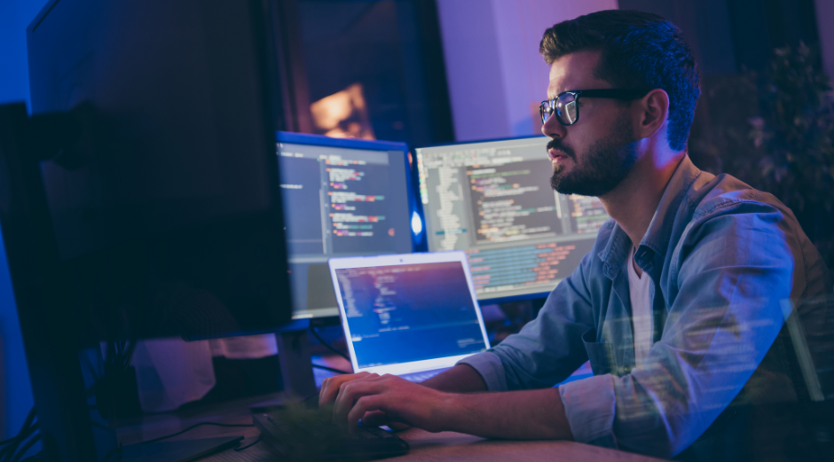 Image of a man sitting at a desk with multiple screens in front of him